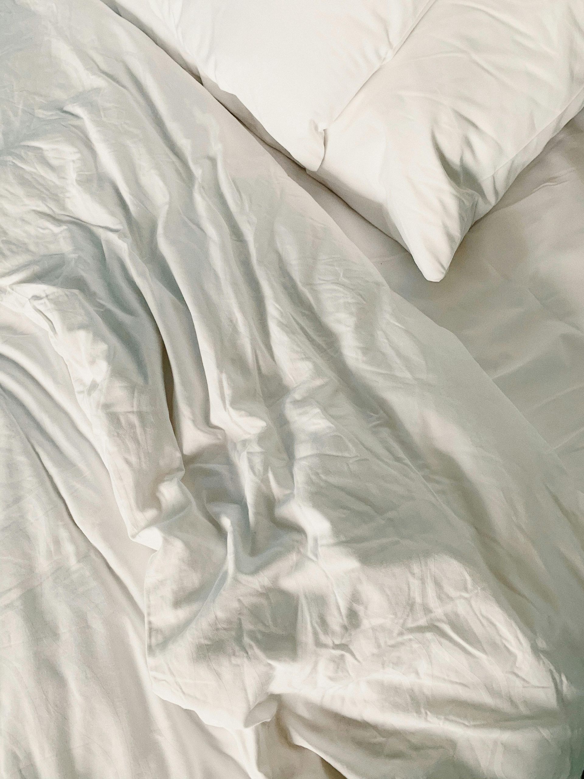 A bed with white sheets and pillows on it.