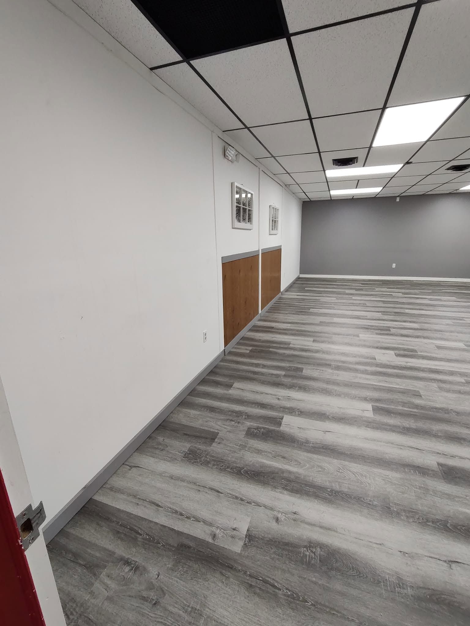 Empty office hallway with white walls, gray carpet, and brown cabinets along the left side.