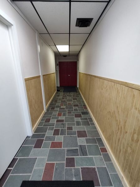 Narrow hallway with patterned carpet, white walls, wood paneling, and a red door at the end.