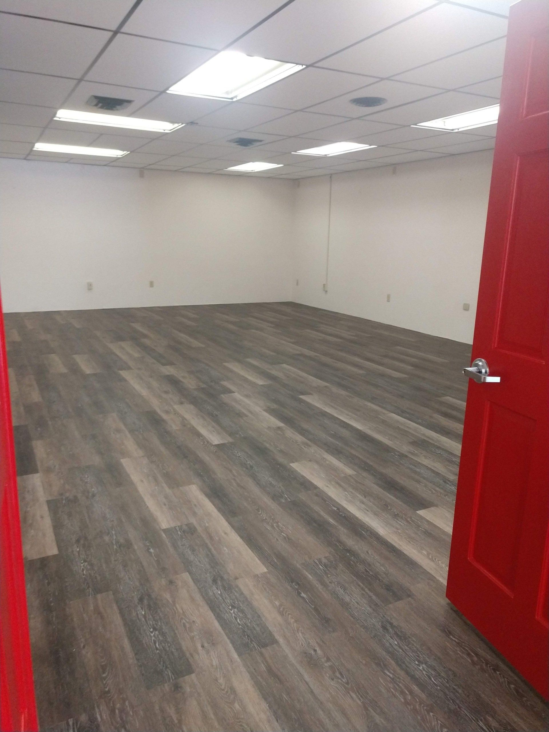 Empty room with gray wood flooring, white walls, and an open red door