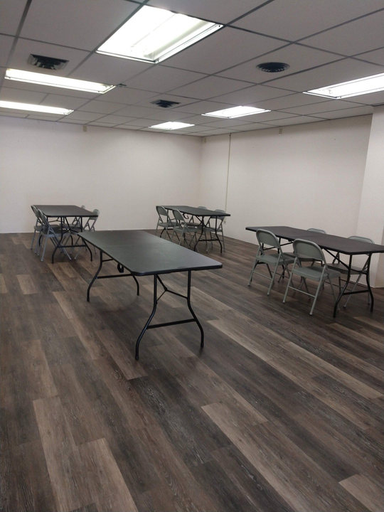 Empty room with folding tables and chairs on a wood floor under fluorescent ceiling lights