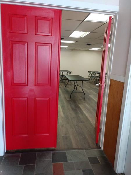Red double doors open to a room with tables and chairs and a tiled floor.