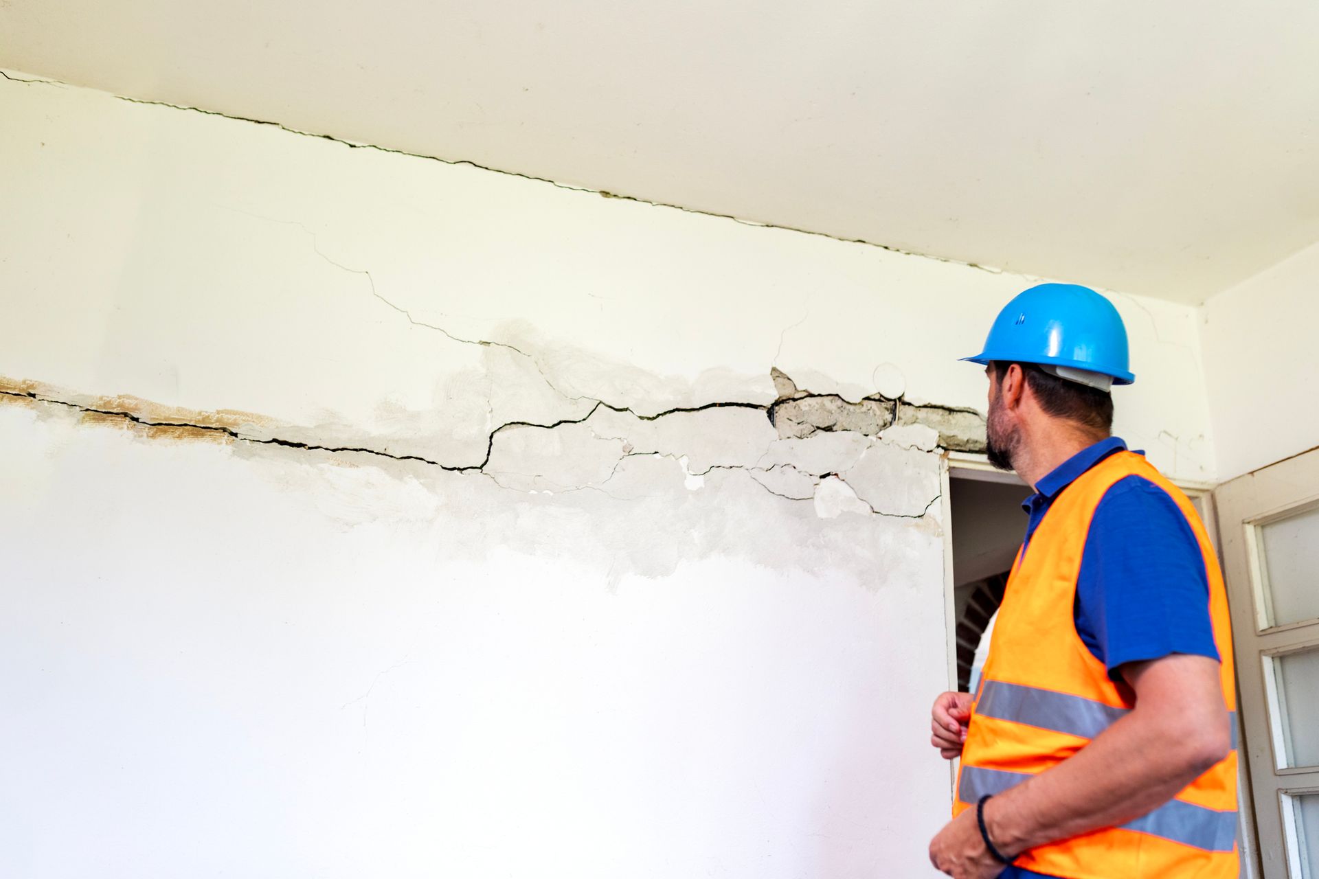 A man in orange vest examines cracked wall for water damage restoration service.