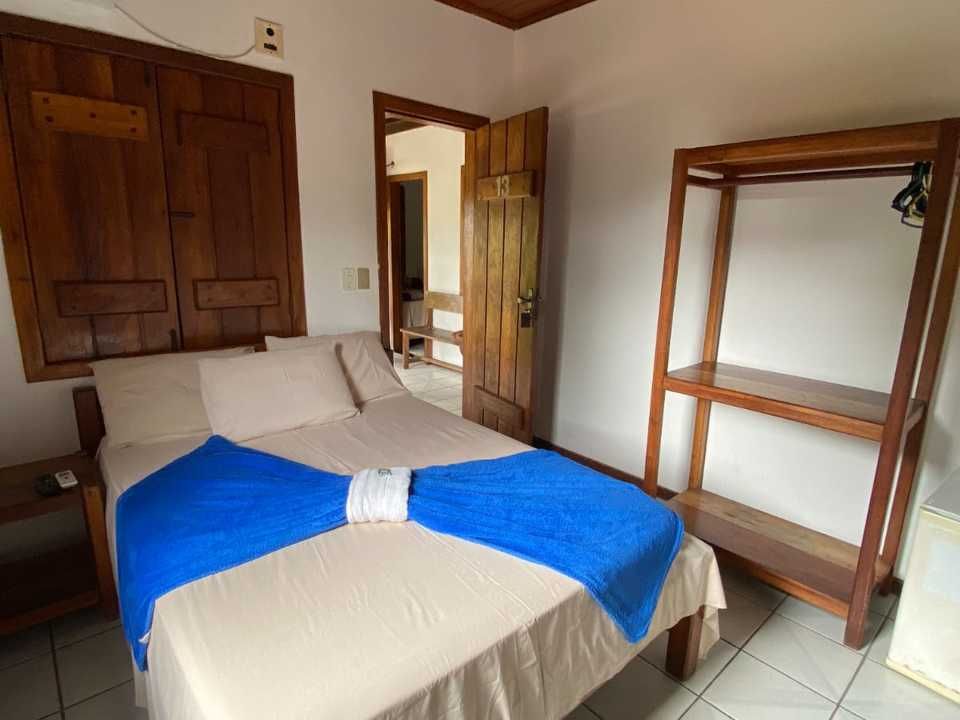 Um quarto arrumado com uma cama de casal, uma toalha azul vibrante, uma porta de madeira e um cabideiro de madeira de conceito aberto.