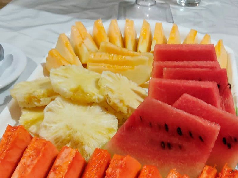 Uma travessa de frutas frescas fatiadas, incluindo melancia, abacaxi, mamão e melão, dispostas em um prato branco.