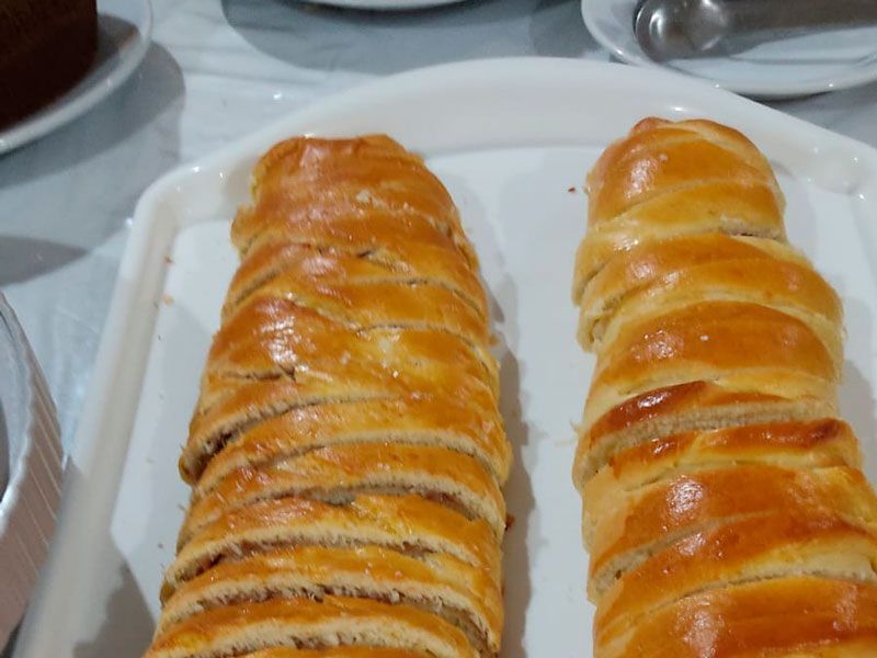 Dois pães trançados dourados, cortados em fatias uniformes, estão dispostos em uma bandeja branca.