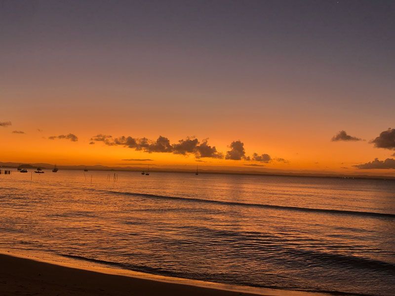 Pôr do sol dourado sobre um oceano calmo com pequenas nuvens dispersas no horizonte, visto de uma praia de areia.
