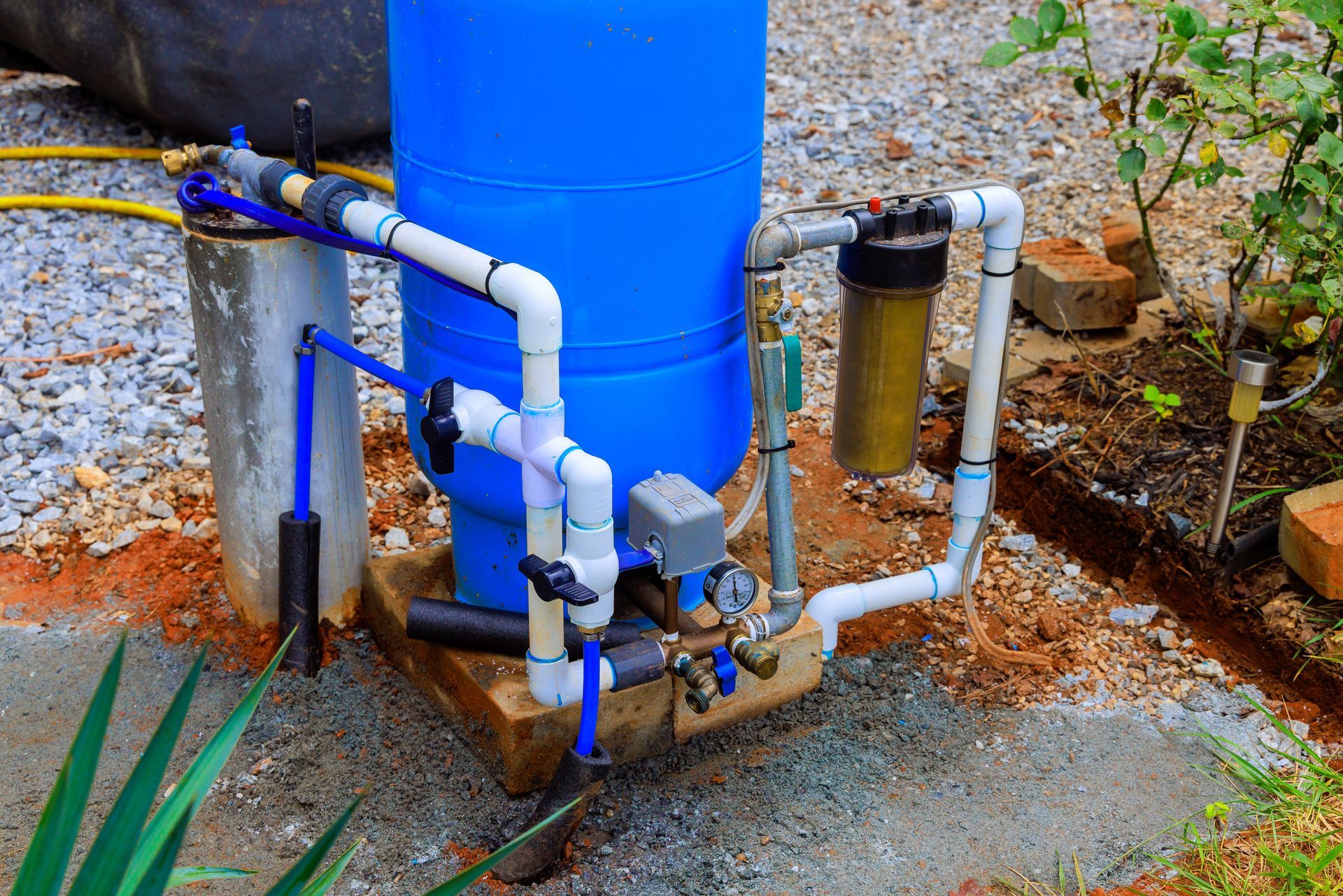 Outdoor water filtration system with blue storage tank, PVC piping and pressure gauge. Outdoor water filtration system with blue storage tank, PVC piping and pressure gauge.