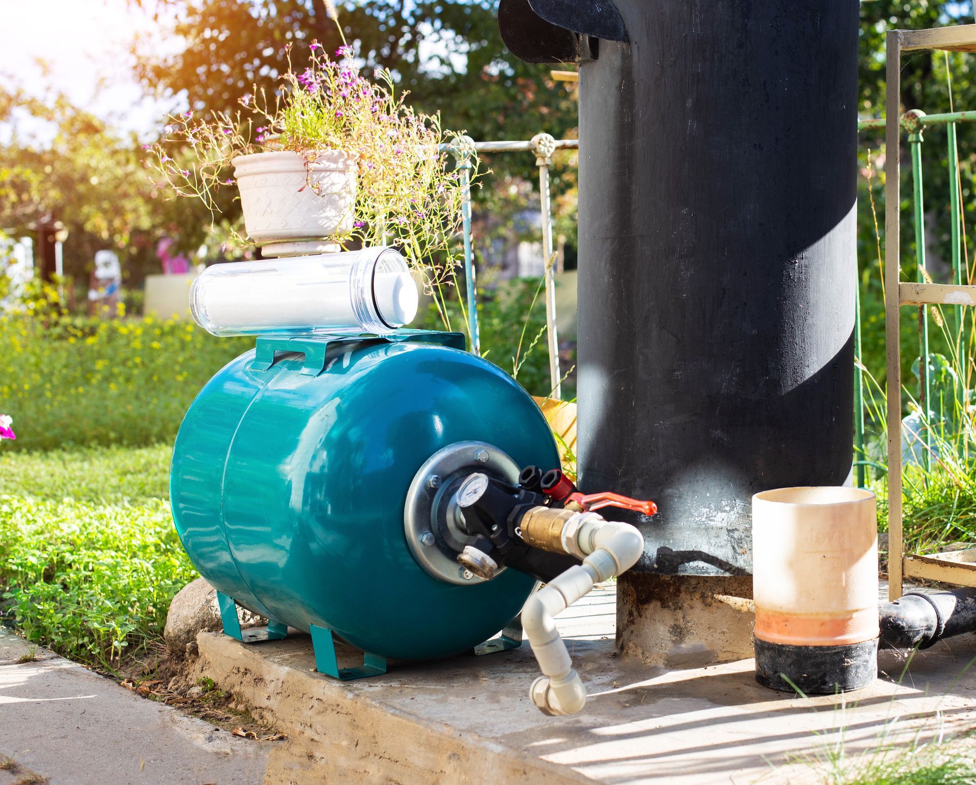 Blue water pressure tank with white components, near a black tank in a sunny outdoor setting.