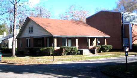 A house with a porch and a brick building in the background