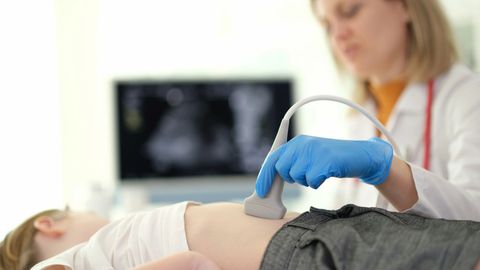 Un operatore sanitario con guanti blu esegue un'ecografia all'addome di un bambino in un contesto clinico.