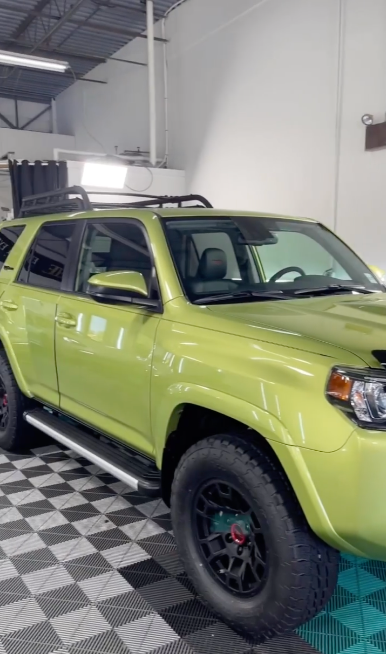 A green suv is parked in a garage on a checkered floor.