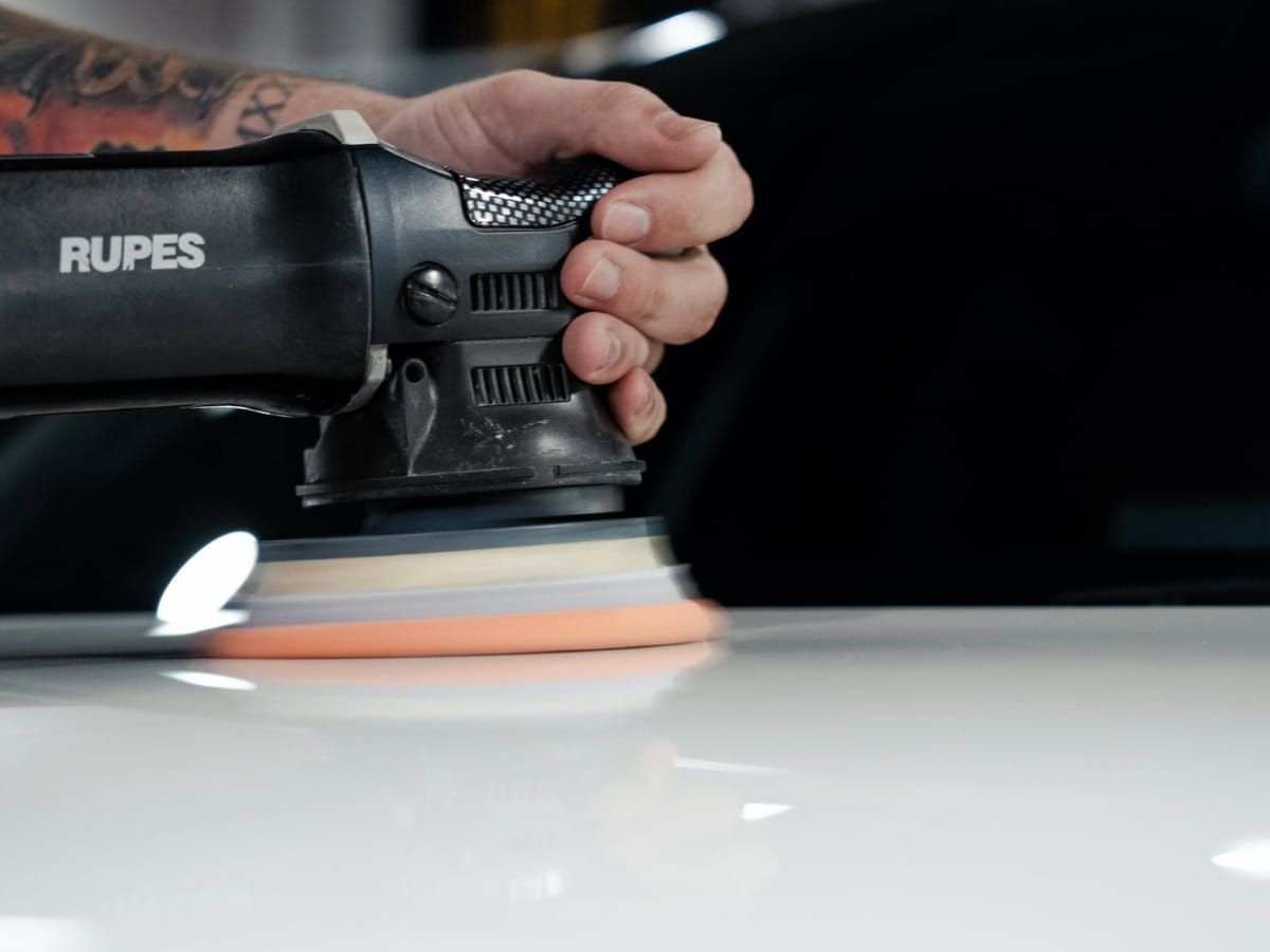 Close-up of a Rupes polisher being used on a white vehicle’s paint.