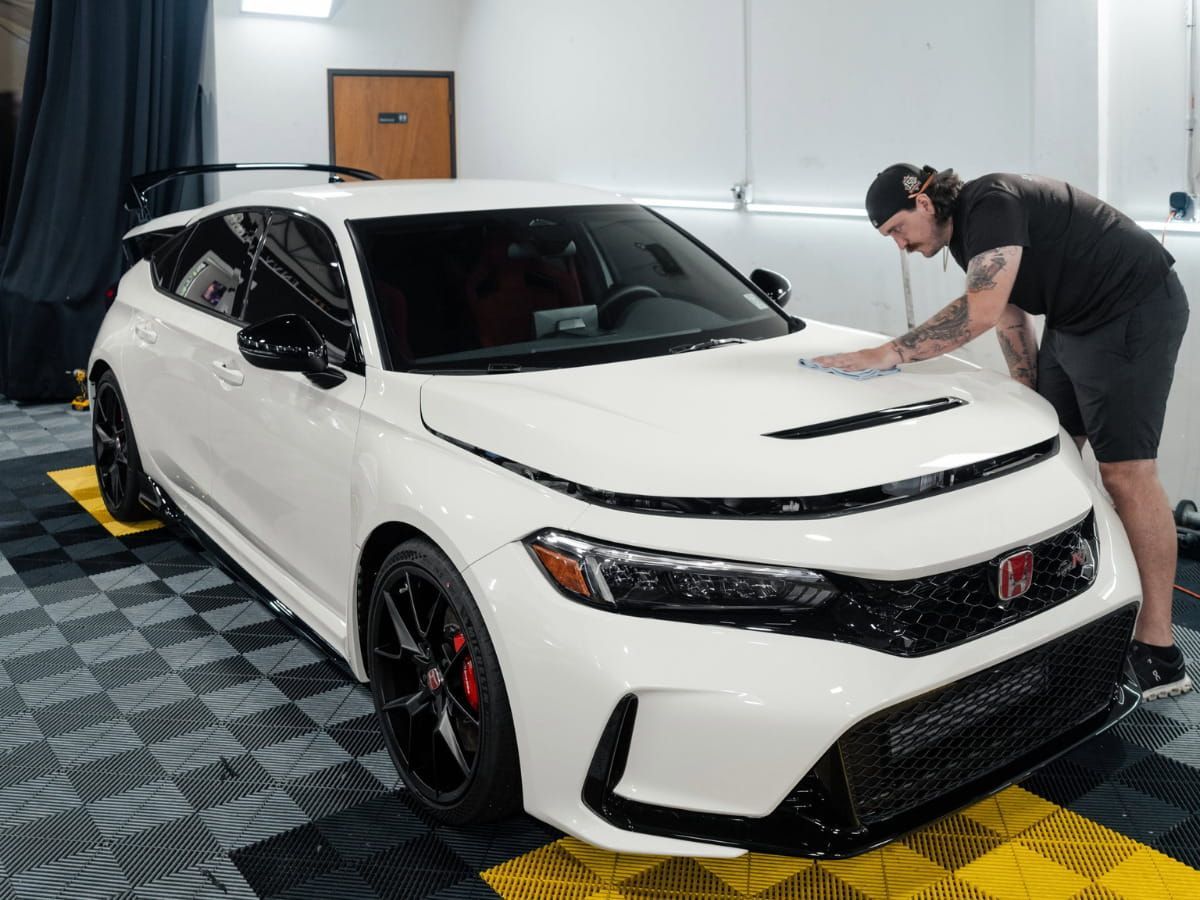 Detailing technician cleaning the hood of a white Honda Civic Type R inside a professional detailing studio.