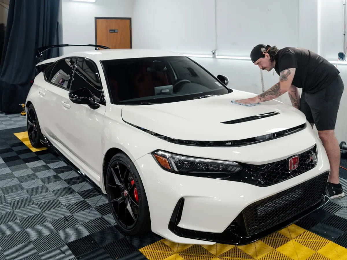 Technician wiping the hood of a white Honda Civic Type R inside Envy Executive Automotive Protection