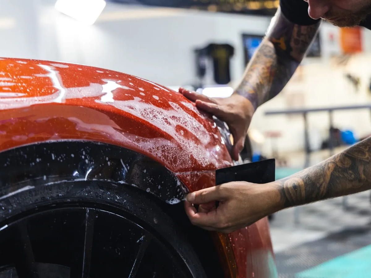 Technician installing paint protection film on the front fender of a red vehicle.
