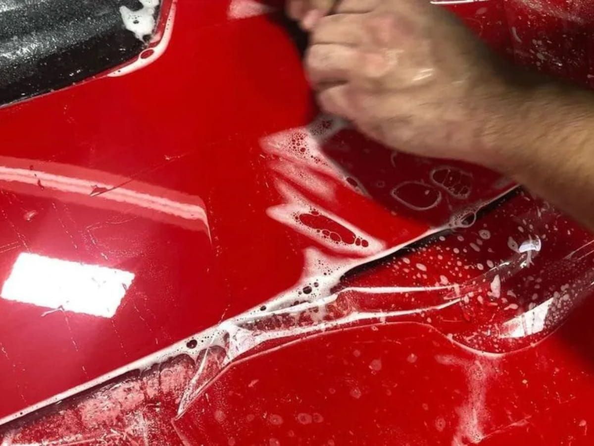 Paint protection film being applied to a red vehicle with installation solution on the surface.