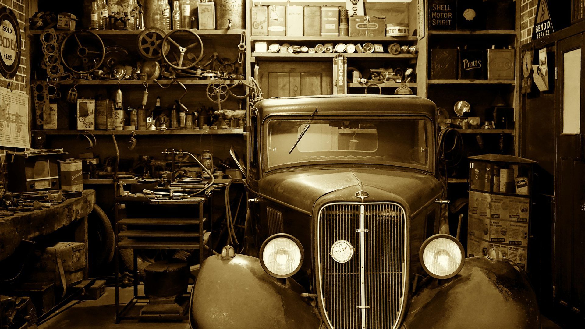 Vintage car in a cluttered workshop, filled with tools and parts, sepia tone.