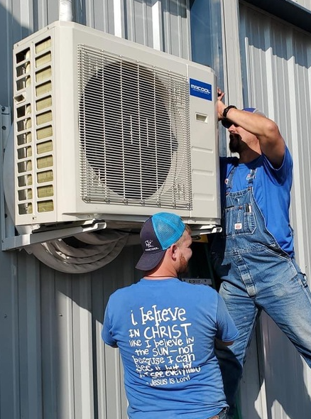 Two workers installing an air conditioning unit on a building.