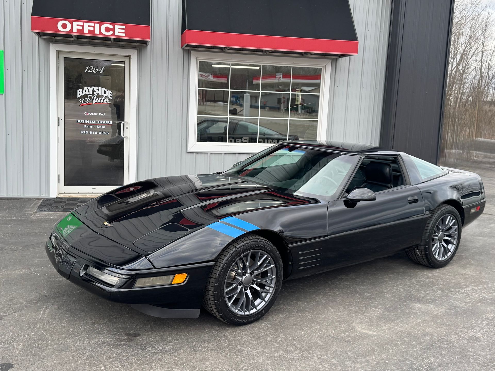 Black Corvette with blue stripes parked outside a building with an