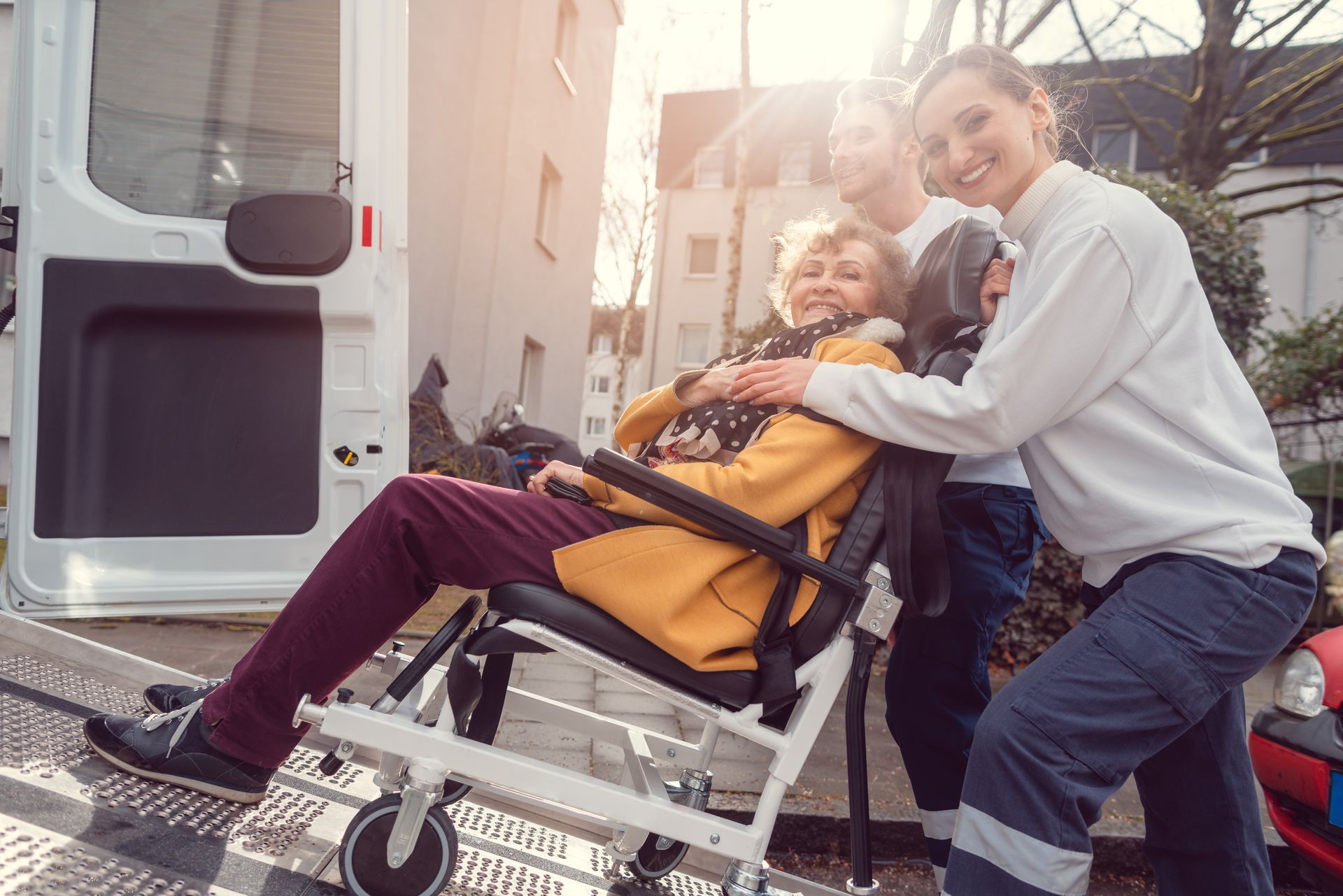 Person in a wheelchair smiling beside an adult outdoors near a vehicle ramp
