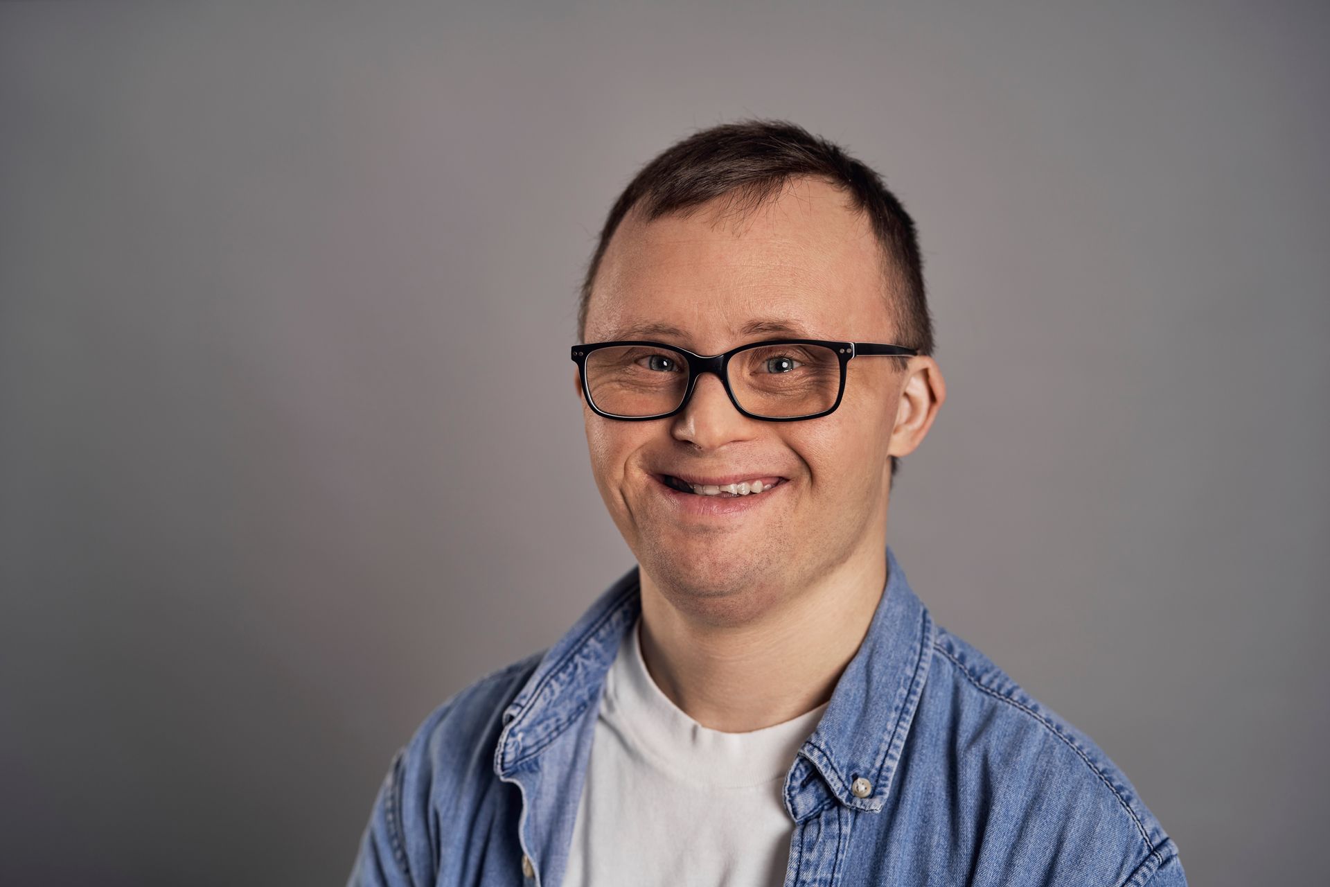 Smiling person wearing glasses and a blue shirt against a gray background