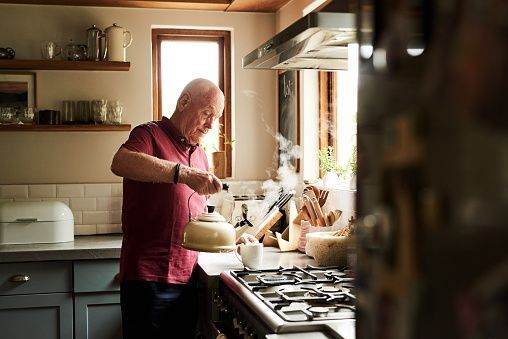 Person cooking in a sunlit kitchen, stirring a pot at the stove.