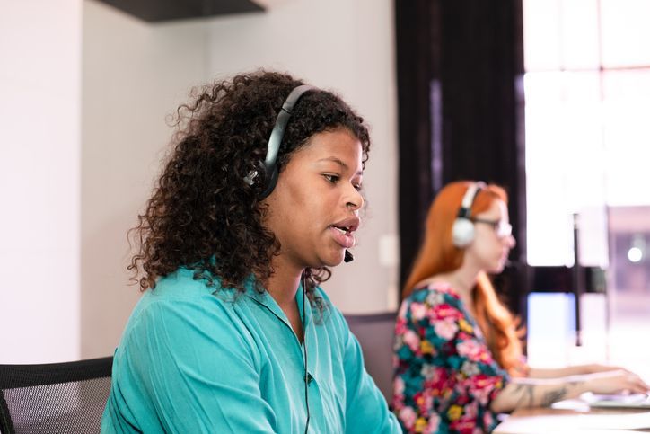 Two women wearing headsets working at computers in an office