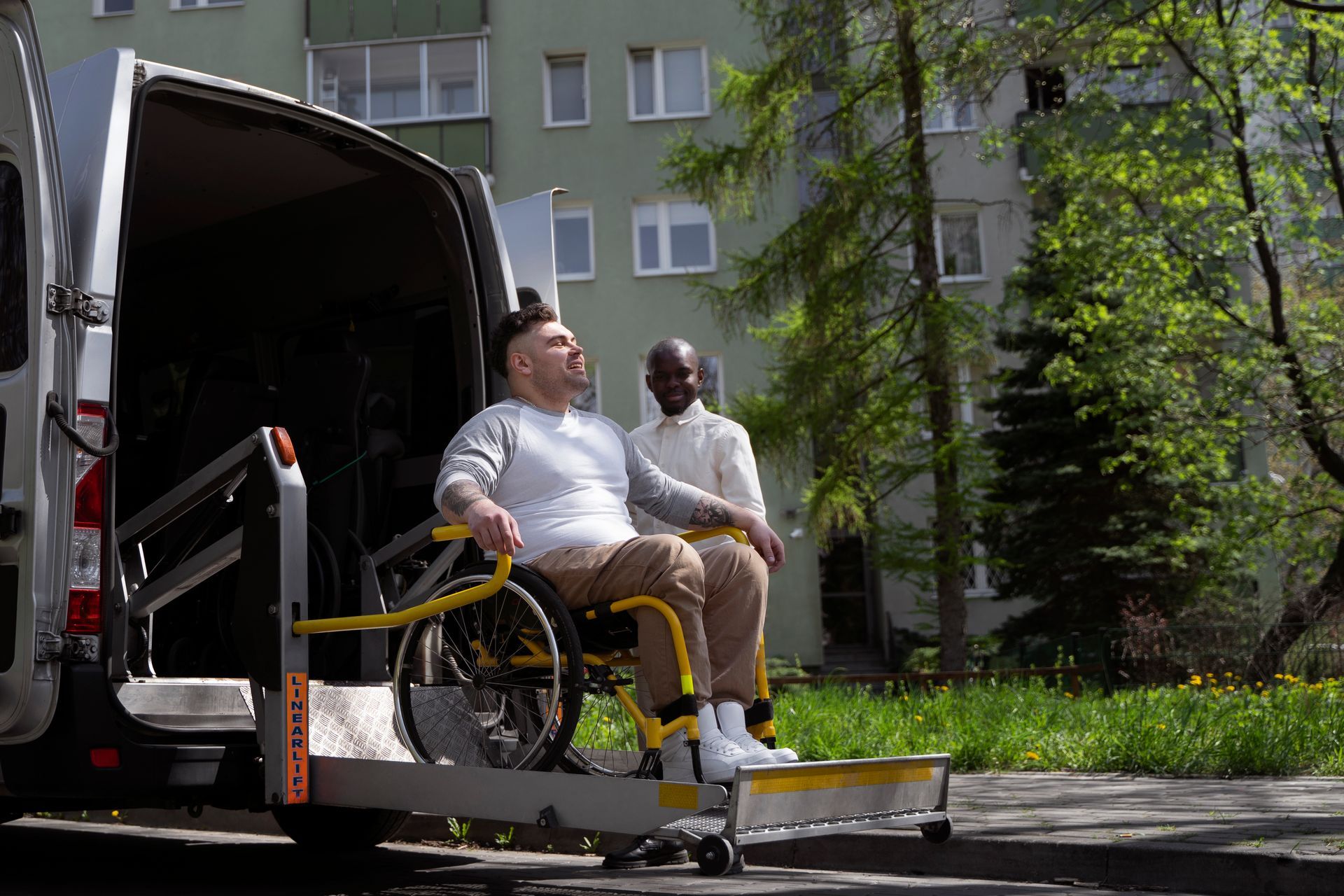 Wheelchair user and attendant on a van lift outside an apartment building