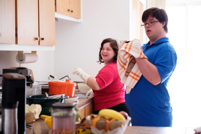 Two people cooking in a bright kitchen, smiling while drying dishes and standing by the counter.