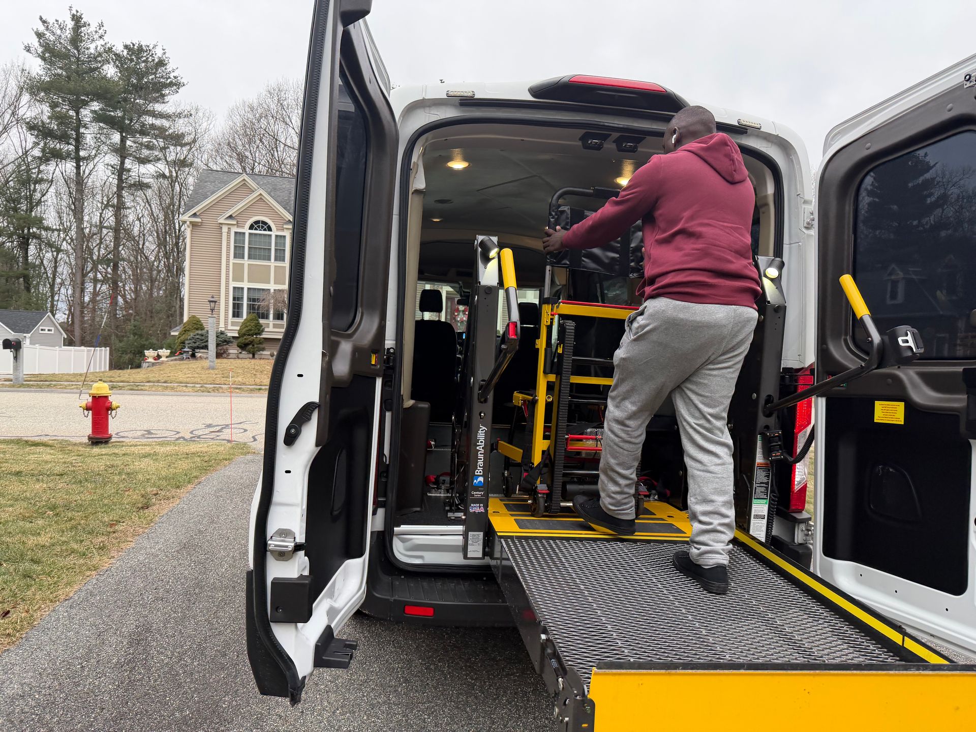 Person in maroon hoodie operating a wheelchair lift on a van in a driveway