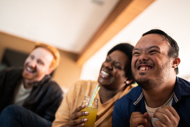 Three smiling friends laughing together indoors, one holding a yellow drink