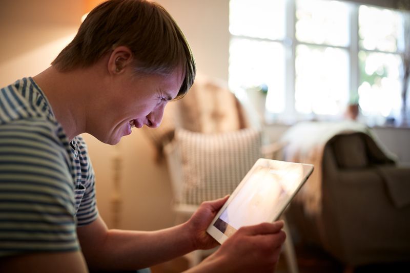 Person smiling while looking at a tablet in a bright living room