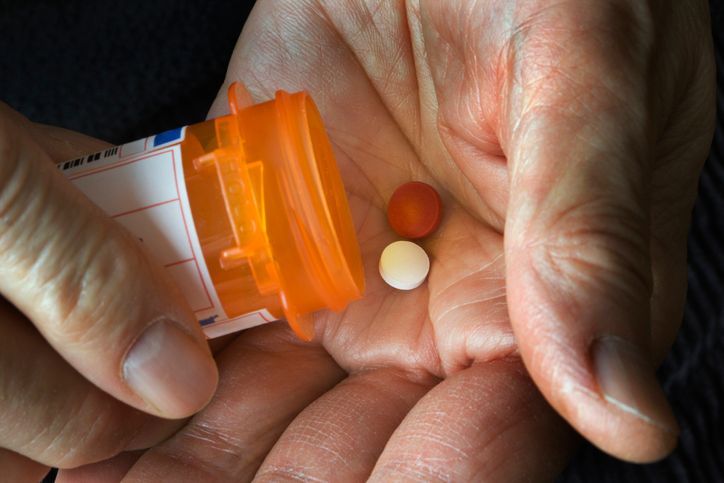 Hands holding an orange pill bottle and two tablets, one white and one orange.