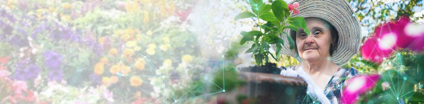 Smiling person in a floral hat tending vibrant flowers in a sunlit garden