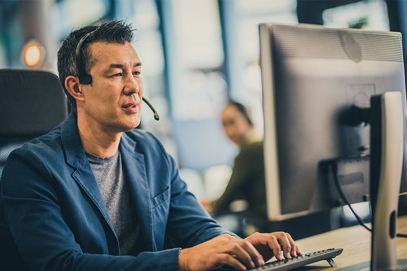 Man working at a desktop computer in an office, wearing a blue blazer and focused on the screen