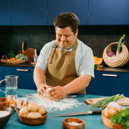 Person kneads dough at a kitchen counter with eggs, vegetables, and utensils nearby