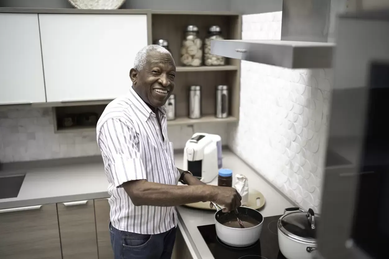 Man cooking in a modern kitchen, stirring a pot and smiling at the counter.