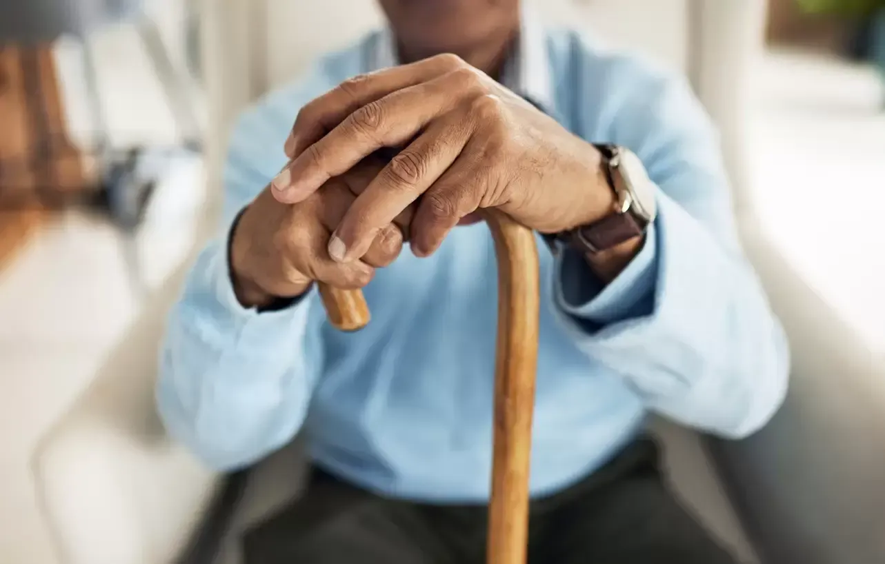 Hands resting on a wooden cane, wearing a light blue shirt.