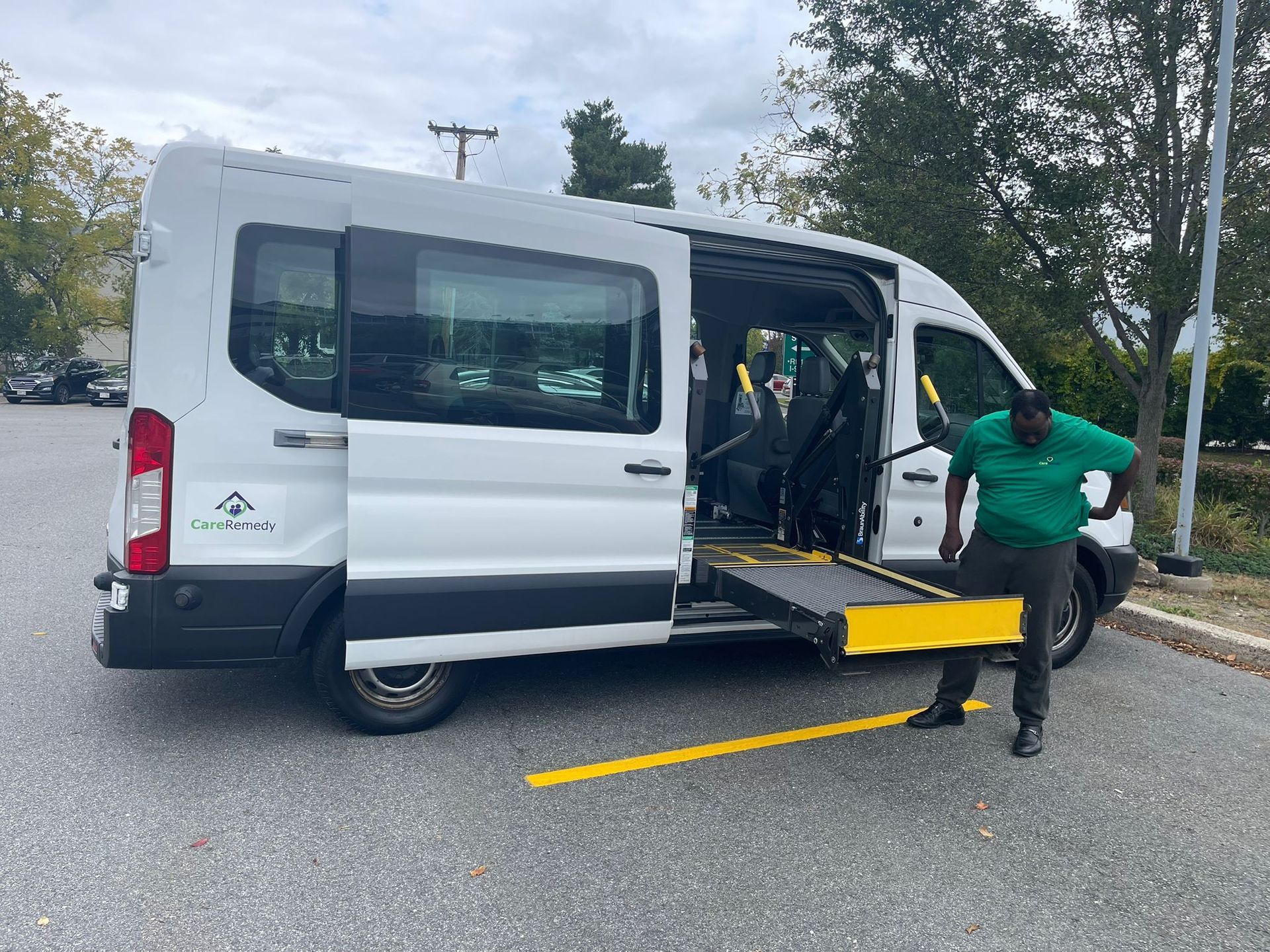White van with wheelchair lift extended; man in green shirt stands beside it on a street.