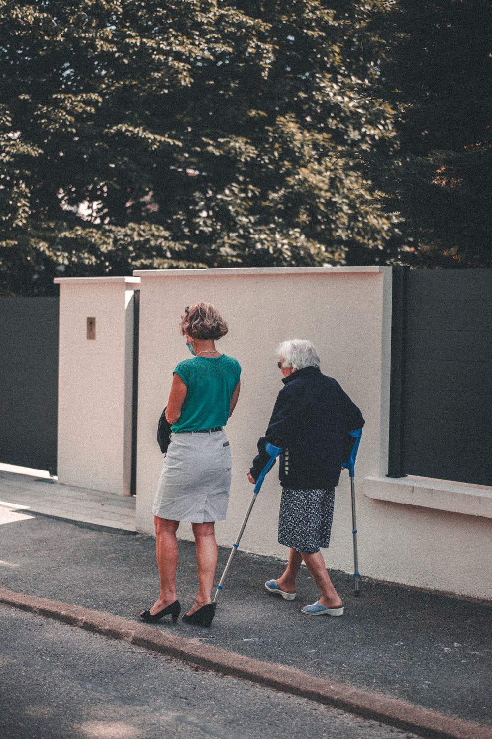 An older woman walking outdoors alongside a companion on a sunny day
