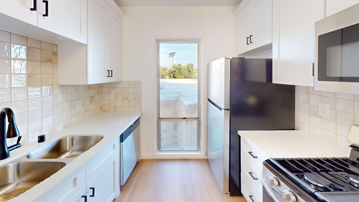 Bright modern white kitchen with stainless appliances and a glass door at the end