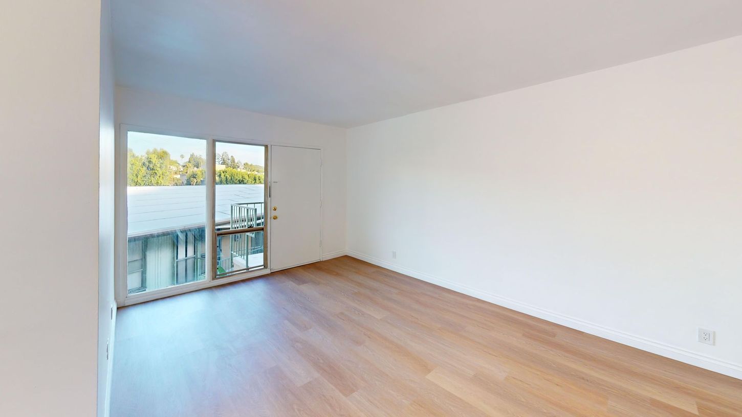 Empty bright living room with wood floors and sliding glass doors to a balcony overlooking water.