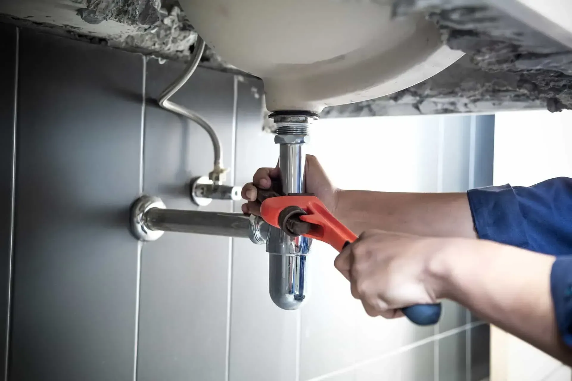Hands using a red pipe wrench to tighten plumbing under a sink
