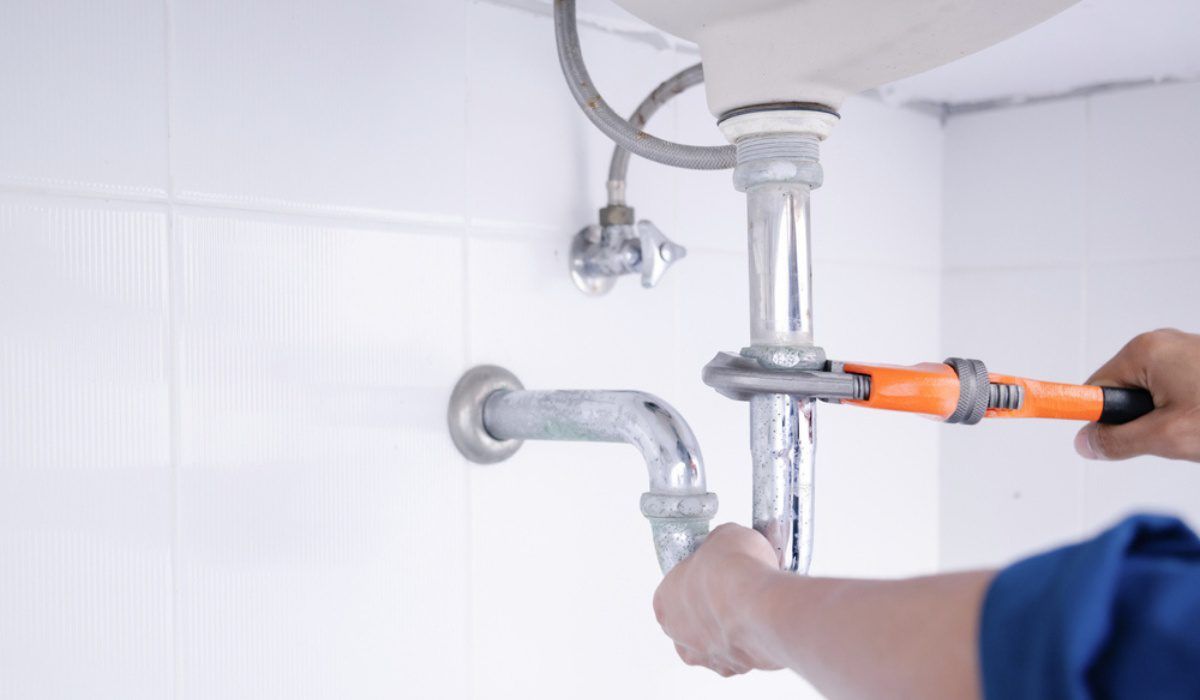 Plumber repairing a sink drain pipe under a bathroom sink with orange tools