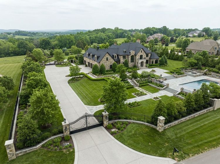 Aerial view of a large stone mansion with a pool, landscaped grounds, and gated driveway.