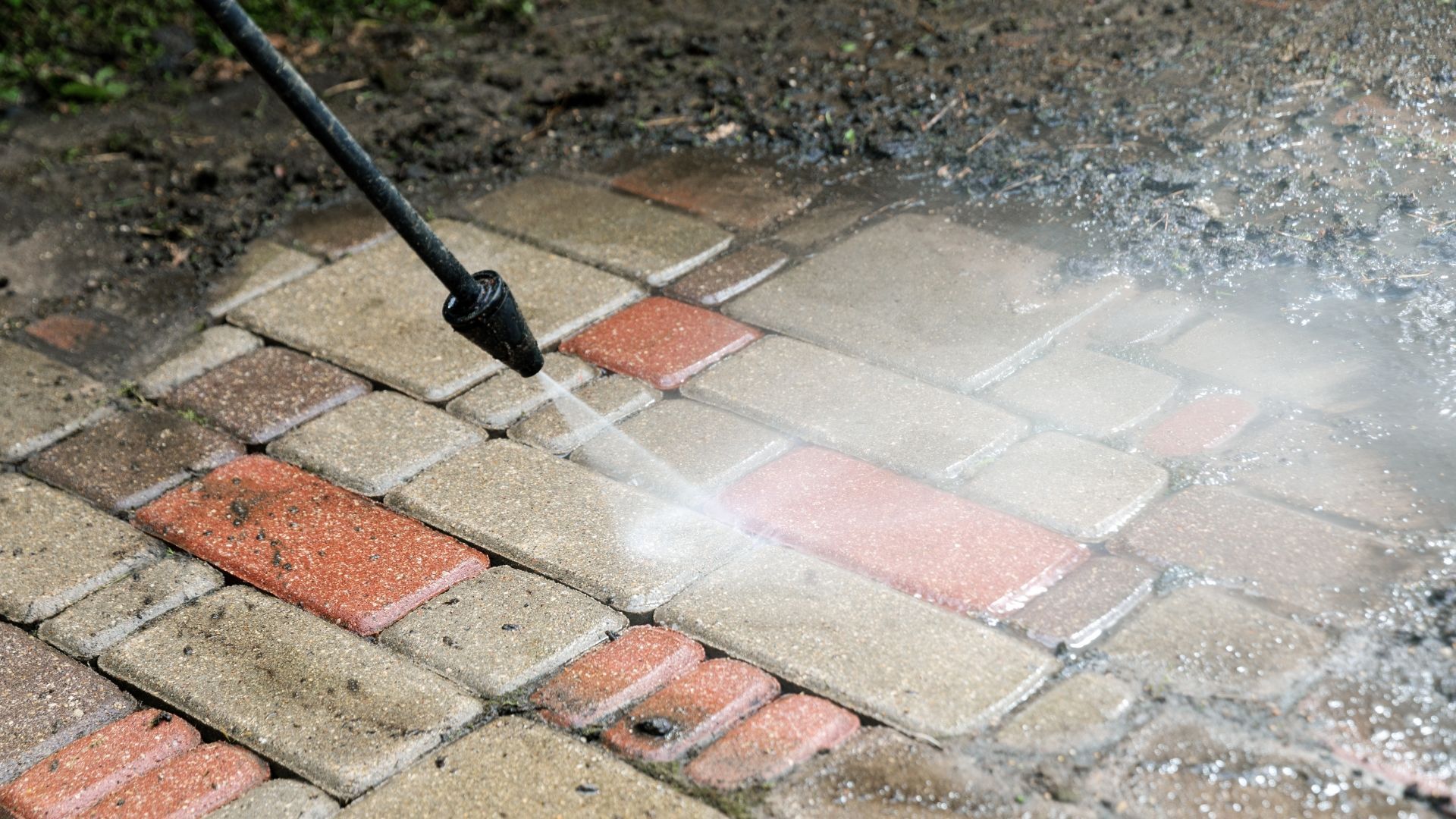 Pressure washer spraying water on a brick patio, cleaning red and tan pavers.