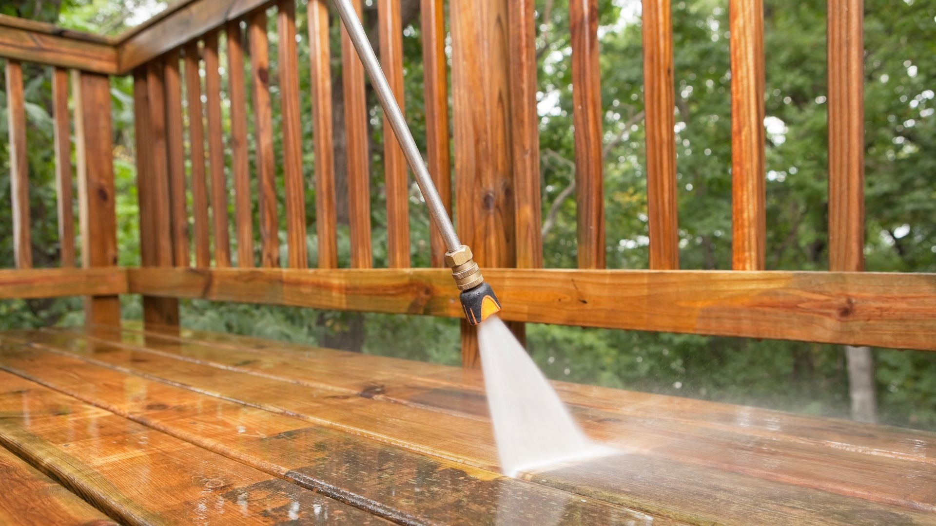 Person pressure-washing a wet wooden deck and railing in the rain
