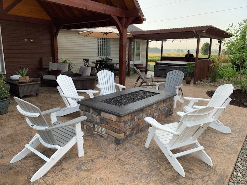 Outdoor patio with Adirondack chairs around a stone fire pit, with a gazebo and hot tub visible.