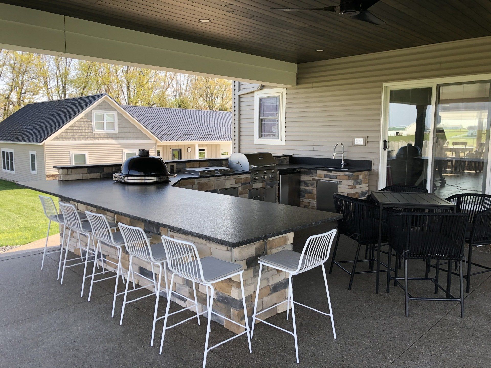 Outdoor kitchen with bar seating, grilling area, and dining table under a covered patio.